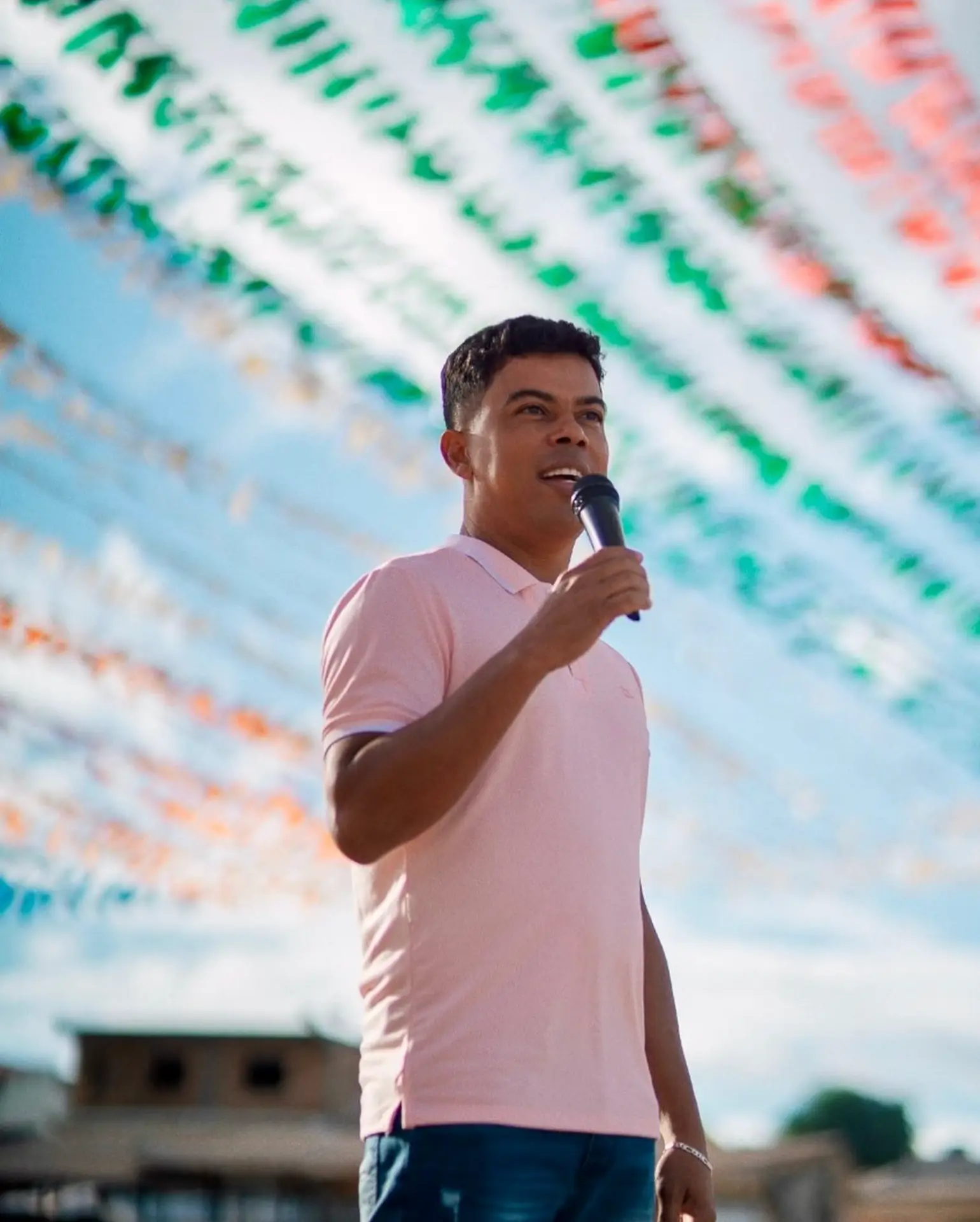 Nilson Santos segurando microfone durante apresentação, sob bandeirinhas de festa
